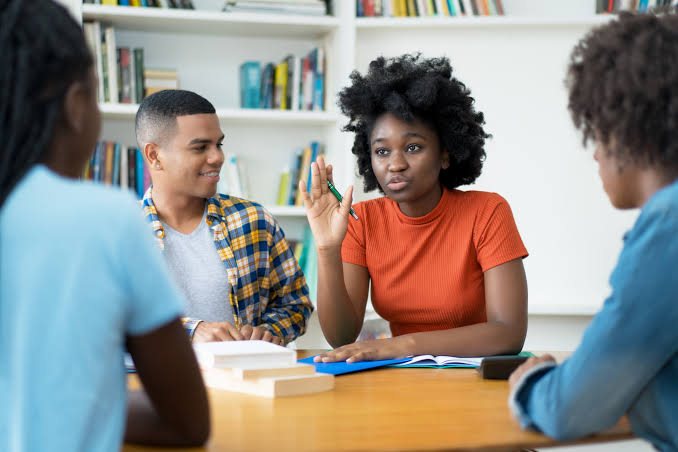 Four young people talking together around a table in a library.